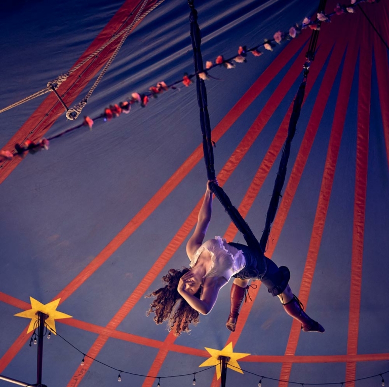 woman hanging from aerial silk under circus tent