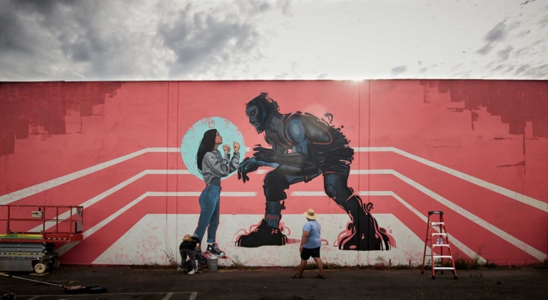 Mural of woman fists up facing robot in boxing ring