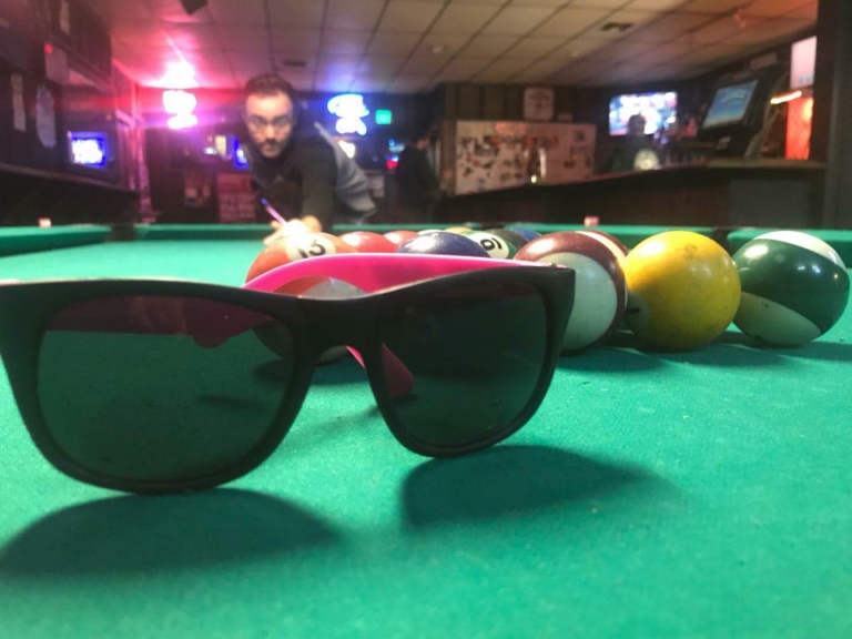 sunglasses sit on a pool table with a person behind it