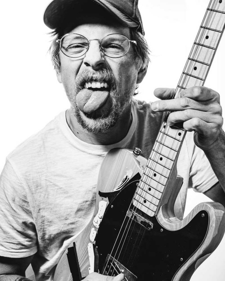 black and white photo of man holding guitar making a face